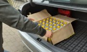 policjant wyciąga karton z butelkami alkoholu z bagażnika samochodu