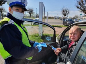 policjantka daje własnoręcznie uszytą maseczkę kierowcy samochodu.&quot;&gt;
