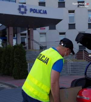 policjant ubrany w kamizelkę odblaskową i ubranie cywilne nosi pudełka z zawartością alkoholu przemysłowego do nieoznakowanego radiowozu