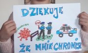 dziewczynka trzyma rysunek z napisem dziękuję, że mnie chronisz, radiowozem policyjnym i dwoma policjantami