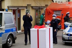 Policjant z megafonem obok dużej paki stylizowanej na prezent