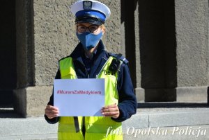 policjant trzyma kartkę z napisem #murem za medykiem&quot;&gt;