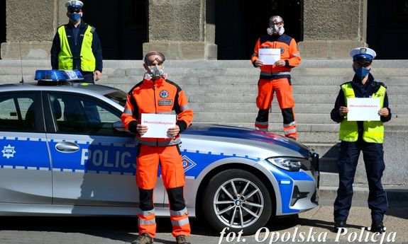 policjanci i ratownicy medyczni stoją obok siebie w ręce trzymając kartkę z napisem #murem za medykiem&quot;&gt;