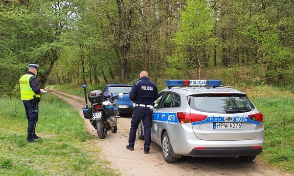 dwaj policjanci, auto, którym uciekał kierujący i policyjny motocykl na leśnej drodze