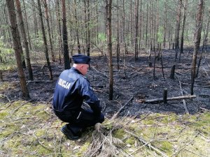 policjant kucający przy fragmencie pogorzeliska