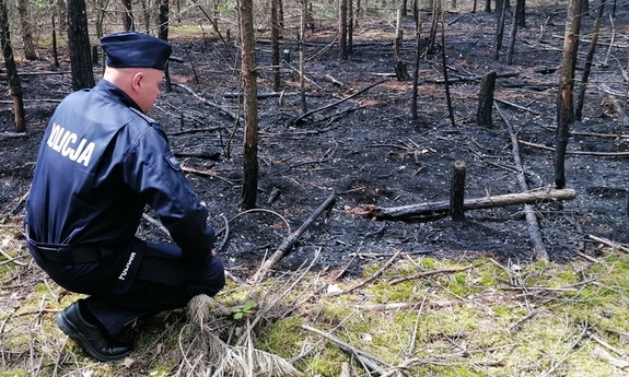 policjant kucający przy fragmencie pogorzeliska