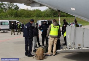 grupa policjantów i funkcjonariuszy w ubraniach cywilnych przed samolotem
