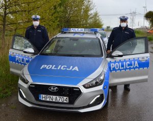 dwaj policjanci w mundurach i w maseczkach przy radiowozie