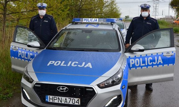 dwaj policjanci w mundurach i w maseczkach przy radiowozie