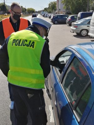 Policjant wręcza nagrodzonemu kierowcy upominek. W tle przedstawiciel Bydgoskiego Zarządu Dróg Miejskich i Komunikacji Publicznej