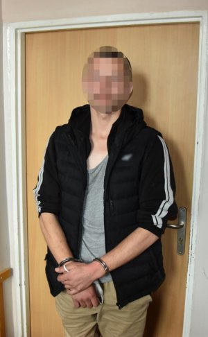 zatrzymany przez policjantów mężczyzna stoi w kajdankach