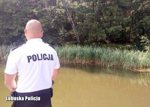 policjant podczas przeszukiwania brzegu jeziora