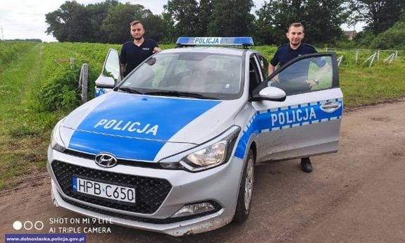 dwaj policjanci stoją przy radiowozie