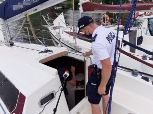 Policjant stojący na jachcie podczas kontroli instalacji przez strażaka wewnątrz jachtu.&quot;&gt;