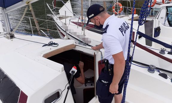 Policjant stojący na jachcie podczas kontroli instalacji przez strażaka wewnątrz jachtu.&quot;&gt;