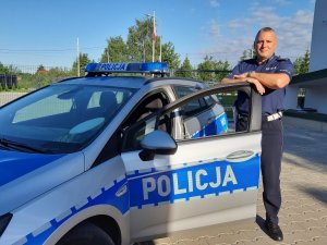 policjant stoi obok zaparkowanego radiowozu, w tle budynek KPP Siemiatyczach