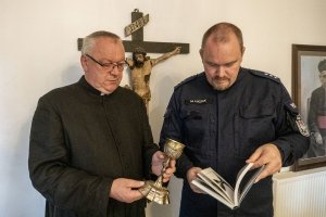 policjant stoi z księdzem, który trzyma odzyskany zabytkowy kielich