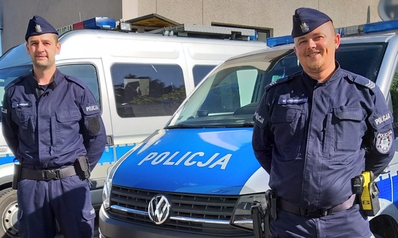 dwaj policjanci, w tle radiowozy policyjne