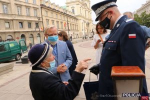 Zastępca Komendanta Głównego Policji rozmawia ze starszą kobietą, obok inni goście otwarcia wystawy