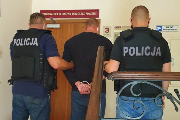 policjanci prowadzą zatrzymanego w kajdankach