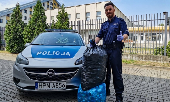 policjant stoi obok radiowozu policyjnego z dwoma workami wypełnionymi nakrętkami