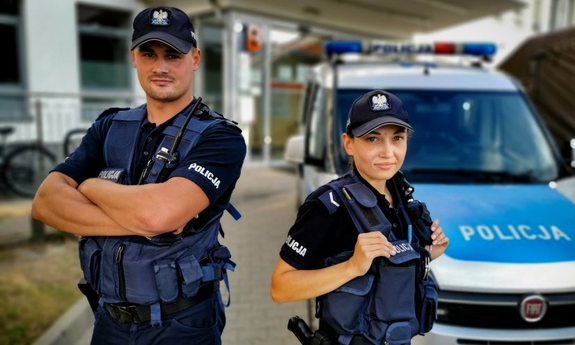 policjant i policjantka stoją przy radiowozie