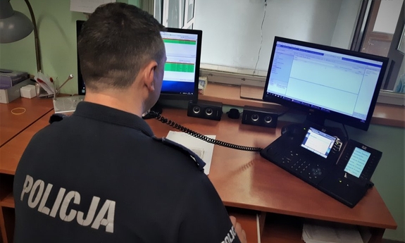 policjant dyżurny siedzi przy stanowisku i rozmawia przez telefon