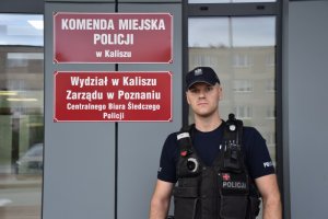 policjant stoi na tle budynku Komendy Miejskiej Policji w Kaliszu