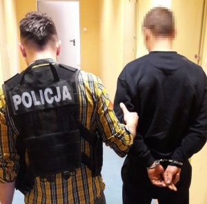 policjant prowadzi zatrzymanego mężczyznę w kajdankach