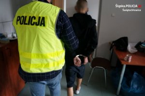 zatrzymany mężczyzna zakuty w kajdanki podczas doprowadzenia przez policjanta z wydziału kryminalnego na przesłuchanie w jednostce Policji