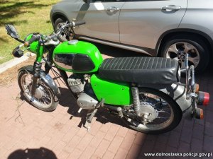 Na zdjęciu odzyskany seledynowo czarny motocykl, w tle srebrny samochód