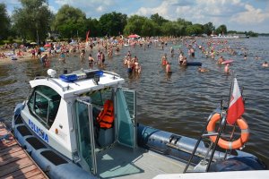 na pierwszym planie łódź policyjna zacumowana przy pomoście, w tle ludzie wypoczywający na plaży