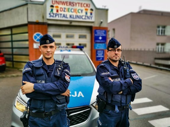 dwaj policjanci stoją przed radiowozem