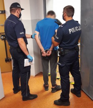 Dwóch policjantów w mundurach stoi przy mężczyźnie w niebieskiej koszulce.&quot;&gt;