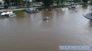 Na zdjęciu motorówka policyjna i łódka na której policjanci przeszukują rzekę. Widok z góry, z drona.