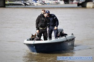 Na zdjęciu Policjanci Komisariatu Wodnego wraz z psem policyjnym znajdują się na łódce i przeszukują rzekę.