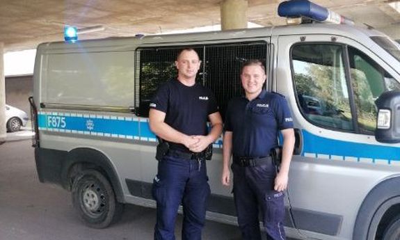 umundurowani policjanci , którzy pilotowali samochód z rodzącą kobietą, stoją przed radiowozem