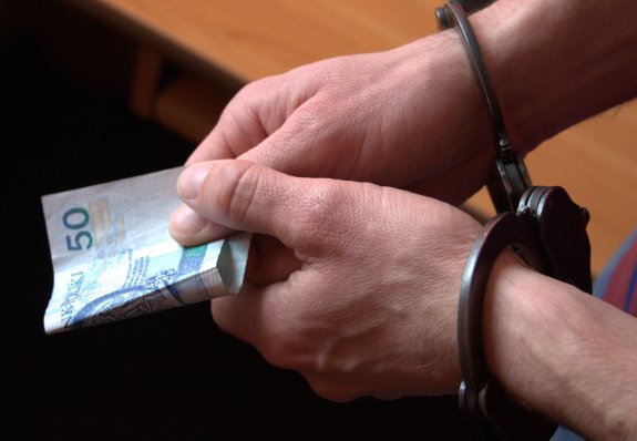 kajdanki na rękach zatrzymanego, który w dłoni trzyma pięćdziesięciozłotowy banknot