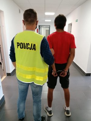 Zatrzymany mężczyzna prowadzony przez policjanta.