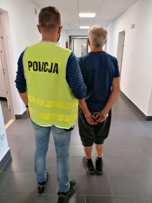 Zatrzymany mężczyzna prowadzony przez policjanta.