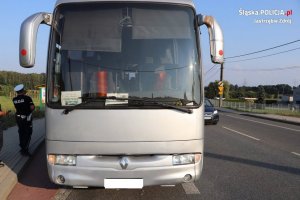 Zdjęcie kolorowe, przedstawiające autobus, obok na chodniku stoi policjant ruchu drogowego
