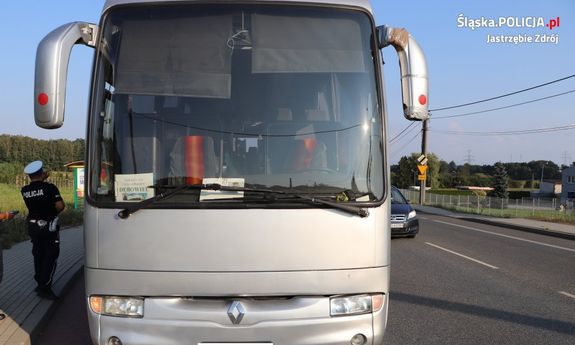 Zdjęcie kolorowe, przedstawiające autobus, obok na chodniku stoi policjant ruchu drogowego