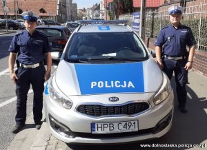 Policjanci, którzy udzielili pomocy osobie poszkodowanej stoją obok radiowozu.