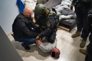 Policjanci zakładają kajdanki zatrzymanemu mężczyźnie, który leży na ziemi.