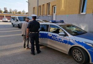 Policjant prowadzi zatrzymanego do radiowozu oznakowanego. Radiowóz stoi na parkingu&amp;quot;&amp;gt;