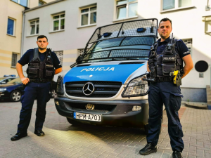 dwaj umundurowani policjanci stoją przy policyjnym radiowozie