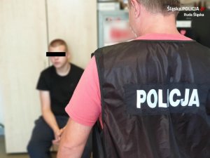 zdjęcie przestawia policjanta kryminalnego odwróconego plecami oraz siedzącego zatrzymanego