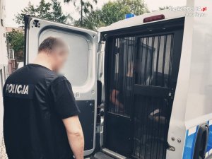 zdjęcie przestawia policjanta kryminalnego z zatrzymanym za kratą w policyjnym radiowozie