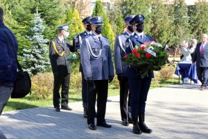 Policjantka trzyma wieniec z tyłu stoi dwóch policjantów