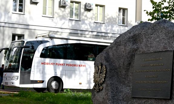 Tablica pamiątkowa na kamieniu przed komendą. W tle krwiobus i budynek komendy.